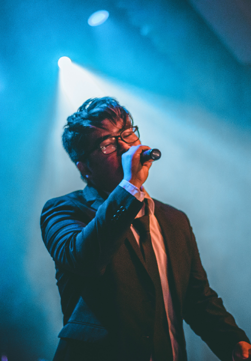 Performer singing on stage under spotlight during a live performance